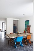 Retro shell chairs in different colours at rustic, wooden kitchen table with frosted glass panel in masonry partition in background