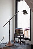 Retro-style, metal standard lamp and storage box on stool in front of tall window in corner