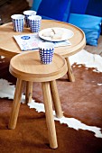 Four blue and white patterned china beakers on two round wooden tables; cowhide rug and blue scatter cushions on floor
