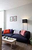 Dunkelblaues Sofa mit bunten Kissen und Stehlampe im Wohnzimmer mit Holzdielenboden