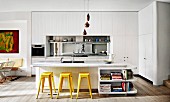 weiße Einbauküche mit verspiegeltem Spritzschutz, Kücheninsel mit Marmor Arbeitsplatte und gelben Retro Barhockern