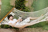 Young man lying in hammock holding tablet computer