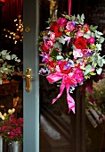 Wreath in various shades of red and pink hanging on glass door with brass fittings