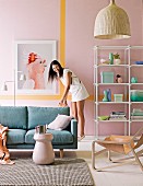 Sofa, open shelving and woman in front of pastel pink wall with yellow stripe