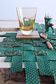 Drinking glass, wooden accessories and fawn figurine on placemat made from green patterned strips of fabric