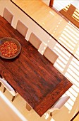 View down onto wooden table, upholstered chairs and pale rug; wooden bowl of dried chillies