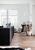 Partially visible cowhide rug on wooden floor in front of dark grey sofa; small workspace next to window in background