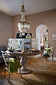 English dolls' house on round wooden table below chandelier in traditional dining room with modern ambiance