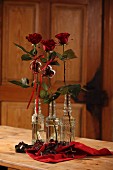 Rote Rosen in Retro Glasflaschen und Weihnachts-Backformen in rotem Tuch auf Holztisch