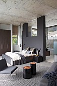 Elegant, purist, designer bedroom with dark grey partition, view into ensuite bathroom with panoramic windows and continuous concrete ceiling