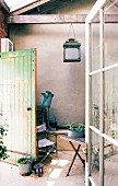 Windfang mit sichtbaren Balken und nostalgischer Laternenleuchte, Gartenmöbeln und bepflanzenten Zinkgefäßen im Vintage-Ambiente
