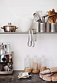 Coffee machine, glass storage jars, bread and butter on worksurface below cooking utensils, containers and tongs on wall-mounted shelf