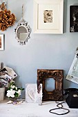 Photo in white frame and mirror on wall above gilt wooden frame and various vintage items on rustic wooden table