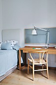 Designer lamp, wooden chair, desk and single bed in simple, minimalist stylish interior