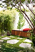 Red cushion on wooden bench in comfortable retreat in summery garden