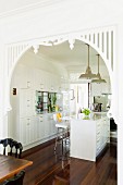 View from dining area into white, country-house-kitchen with white-painted ornate open doorway