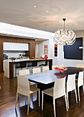Dining table, designer Dandelion pendant lamp and pale plastic chairs in front of breakfast bar in open-plan kitchen