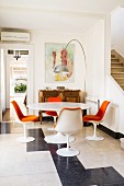 Tulip dining set with orange chair cushions combined with classic arc lamp and small, antique cabinet