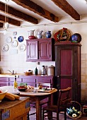 French country-house kitchen with aubergine cupboards and rustic dining area in farmhouse