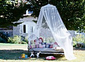 Iron bed with patterned, handmade scatter cushions below draped mosquito net in garden of French country house