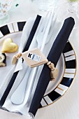 Wooden bead napkin ring with name on stickers around cutlery and black and white linen napkin on patterned plate