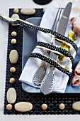 Cutlery and napkin tied with black and gold ribbon on place mat with wooden beads