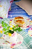 Tasse mit gelben Wiesenblumen vor geblümten Teller mit Focaccia Schnitten im Bett auf Picknickdecke