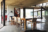 Chairs with woven seats and backrests in dining area in open-plan, contemporary house with glass facade and exposed concrete ceilings