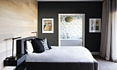 Doppelbett mit Kissenstapel vor gepolstertem Kopfteil an holzverkleideter Wand in elegantem Schlafzimmer und Blick durch offene Tür ins Bad ensuite