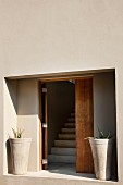 Minimalist entrance area - niche with open wooden front door flanked by concrete planters and view of staircase