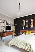 French bed with wooden headboard below skateboards hung on black-painted wall, TV on fifties sideboard below drawings on wall painted pale grey