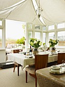Set table below white awnings on ceiling in elegant conservatory with open terrace doors