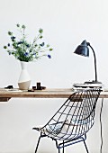 Black, 60s-style, metal wire chair in front of table with simple wooden top and white vase of Nigella damascena