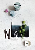 Still-life arrangement of Nigella seed heads on dip-dyed black and white napkin and simple grey china pots on marble surface
