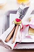 Cutlery and linen napkin in simple napkin ring lovingly decorated with gold bottle cap and heart motif