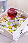 White wooden tray with cup of fruit tea and dish of biscuits arranged on bottle caps painted white and yellow with smiley faces