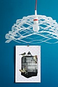 Airy, paper pendant lamp in front of collage of cut-out paper birds and birdcage on blue wall
