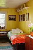 Single bed with colourful bedspread in corner of rustic room painted yellow