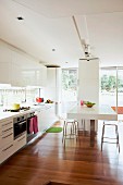 White, designer fitted kitchen with breakfast bar and stools against pillar; elegant walnut parquet floor
