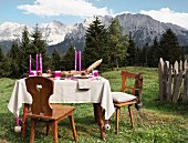 Pinkfarbene Kerzen auf Tisch mit Leinen Tischdecke und rustikalem Flair vor sommerlicher Berglandschaft