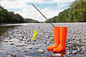 Yellow paper boat hanging from hand-made fishing rod stuck in bright orange wellingtons