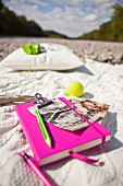 Notebook with pink cover and bright yellow tennis ball on ecru, knitted blanket outdoors