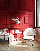 Dark grey metal bed frame, white armchair with matching footstool on white flokati rug in front of red-painted wood-panelled wall
