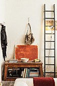 Books and antique sewing machine in open-fronted, vintage wooden cabinet and painted canvas between clip lamp on wooden ladder and coat pegs