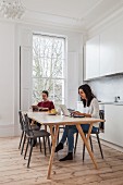 Young couple reading and working on laptop on table in white kitchen-dining room in period apartment with lattice window and wooden floor