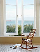Simple wooden rocking chair in front of window with sea view