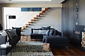 Dark grey sofa set and rug in front of modern open fireplace; staircase with floating wooden treads and delicate balustrade in background