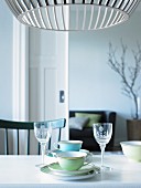 Cups and liqueur glasses on table below Scandinavian designer lamp