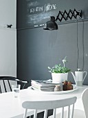 White dining table in front of grey wall with retro-style, black wall lamp