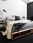 White blanket with pattern of holes on DIY bed with integrated shoe rack in rustic interior with whitewashed brick wall